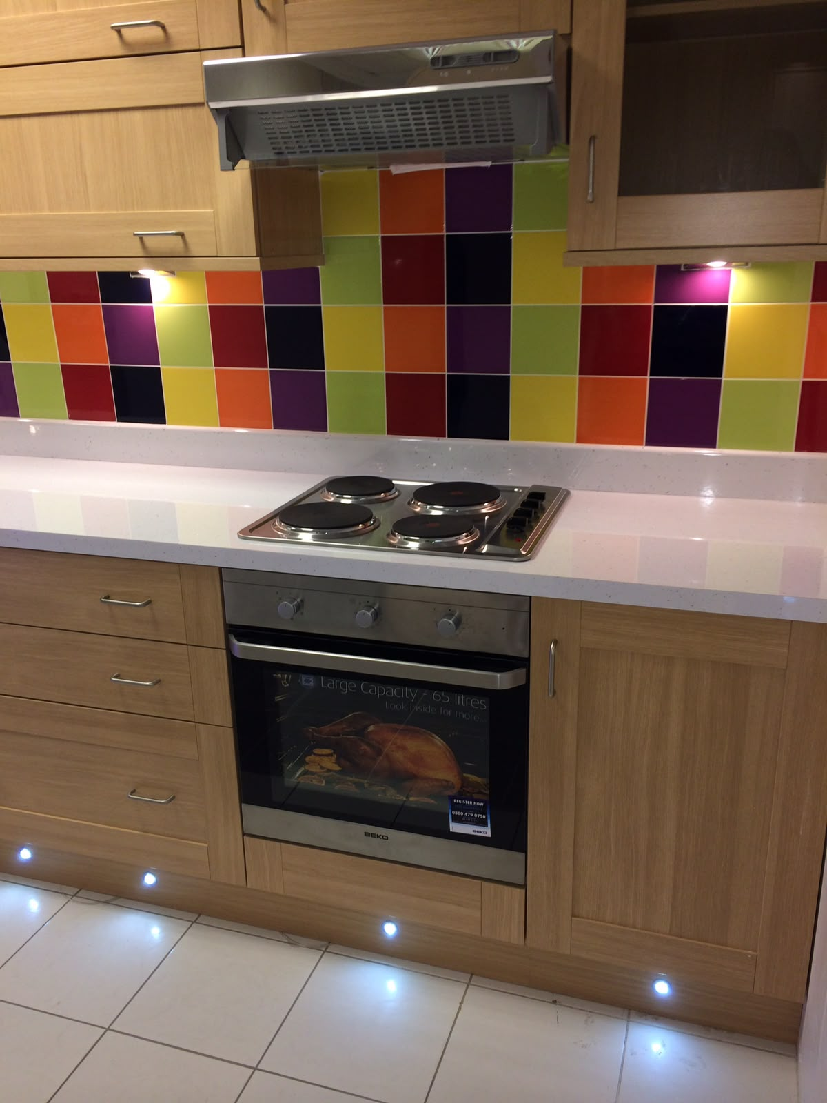 Fitted kitchen with BEKO oven, multicoloured tiled splashback and toe-kick lighting by Aaron Steven Construction