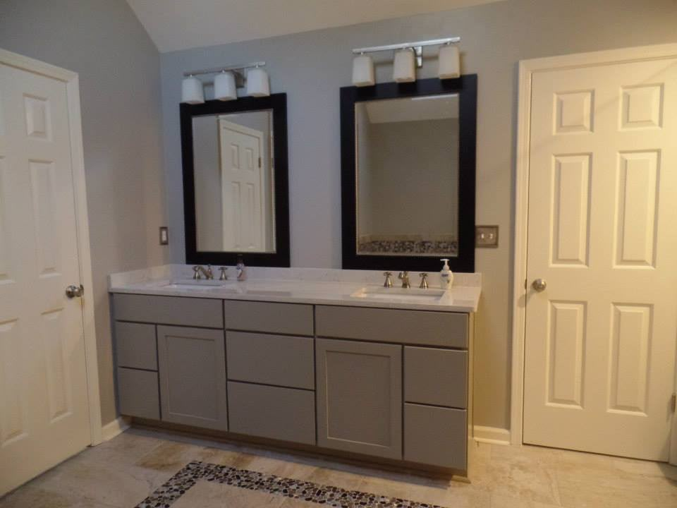 Grey double-sink bathroom vanity between white doors with framed mirrors by Aaron Steven Construction